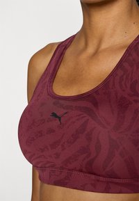 Bordo sportski brus s teksturiranim uzorkom, s crnim logotipom. Dizajn uključuje izrez s raga i debele naramenice za potporu.