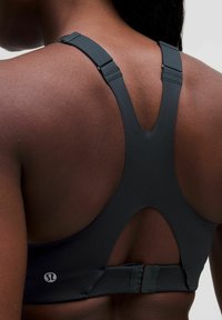 Svart sportbehå, med V-formad rygg, justerbara axelband och spänne. Slät yta med minimal varumärkesdetalj.
