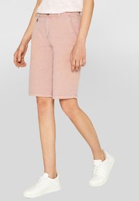 Pantaloni bermuda in cotone rosa chiaro con taglio dritto, tasche frontali e orlo sottile. Abbinati a sneakers bianche.