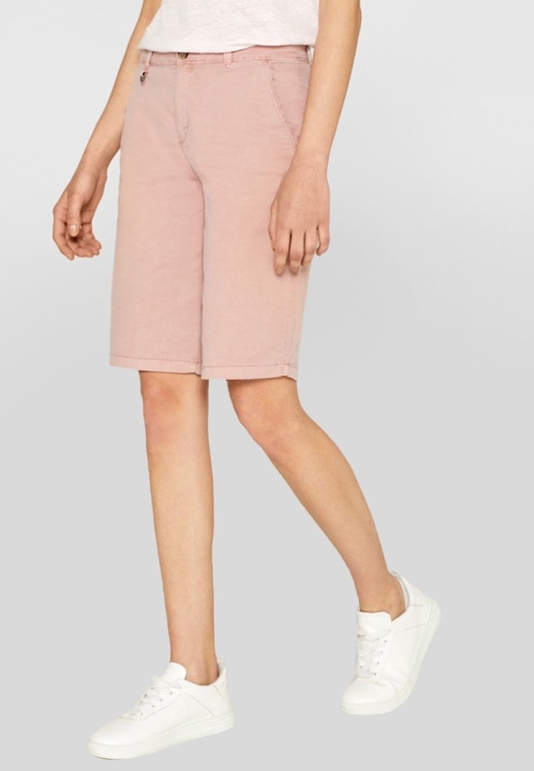 Pantaloni bermuda in cotone rosa chiaro con taglio dritto, tasche frontali e orlo sottile. Abbinati a sneakers bianche.