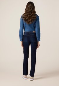 Jean de mezclilla oscura con un corte entallado, con bolsillos traseros y una cinturilla contrastante. Combinado con una camisa de mezclilla azul, de tela texturizada.