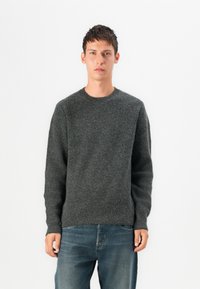Grey knitted sweater with a round neckline and ribbed texture, paired with light blue jeans. The fabric appears soft and warm.
