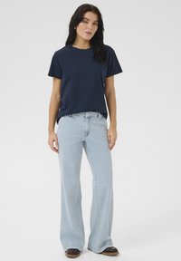 Navy blue cotton t-shirt with short sleeves, paired with light blue wide-leg jeans. Brown footwear with a textured sole.
