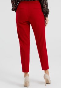 Czerwone zwężane spodnie z gładkiego materiału, z dwoma tylnymi kieszeniami i dopasowaną talią, w komplecie z beżowymi szpilkami.