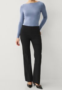 Sininen pitkähihaisen paita, jossa on venepääntie, yhdistettynä mustiin, räätälöityihin suoriin housuihin; ominaisuuksiin kuuluu sileä kangas ja kiiltävät, mustat korkokengät.