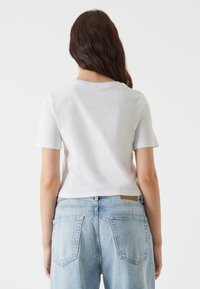 Camiseta de algodón corta blanca con cuello redondo, diseño corto, combinada con unos vaqueros de denim de talle alto azul claro que tienen bolsillos en la parte posterior.