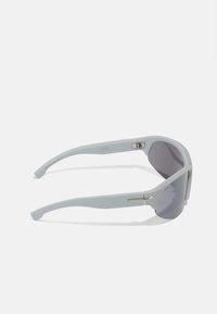 Gafas de sol gris claro con acabado mate y lentes gris oscuro. Presentan acentos metálicos y una forma aerodinámica. Logo impreso en la montura.