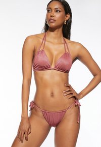 Różowy metaliczny top bikini w kształcie trójkąta z regulowanymi ramiączkami, w komplecie z dopasowanymi majtkami bikini wiązanymi po bokach. Gładka tekstura, minimalne krycie.