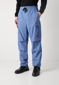 Calças cargo de um azul claro, feitas de tecido, com cintura elástica, cordão e bolsos laterais. Inclui um rótulo em vermelho.