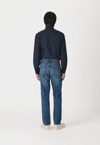 Cămașă albastră cu mâneci lungi, cu guler tip button-down, asortată cu blugi albaștri având o etichetă din piele maro și detalii subtile de cusătură la cusături.