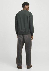 Donkergroene sweatshirt met ribgebreide manchetten en zoom, gecombineerd met loszittende grijze jeans. Eenvoudig ontwerp en textuur, geen zichtbare logo's of patronen.