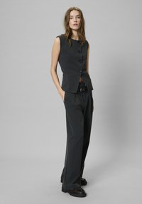 Sötétszürke, csíkos mellény, kerek nyakkivágással és három gombbal, széles szárú nadrággal párosítva. Lapos cipők kiegészítik az öltözéket.