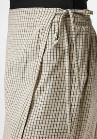 Jupe portefeuille beige avec un motif à carreaux noirs nouée à la taille sur un haut noir, vue de la taille jusqu'au milieu de la cuisse.