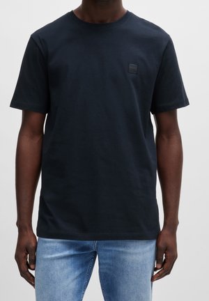 T-shirt bleu foncé à manches courtes avec un petit logo carré "BOSS" sur la poitrine, porté avec un jean bleu clair.
