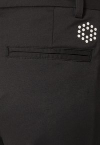 Černé kalhoty s zadní kapsou v elegantním, plošném designu a výrazným logem s bílým puntíkovým vzorem v horním rohu.