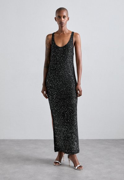 Black sleeveless maxi dress with sparkling texture, side slits, and a scoop neckline, paired with silver strappy high heels.