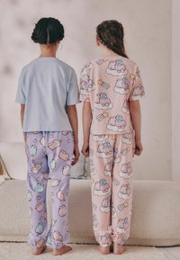 Två barn har på sig matchande pyjamasuppsättningar. Den ena har en ljusblå topp med korta ärmar och lavendelfärgade byxor, den andra har en rosa topp och byxor med ett mönster av en tecknad katt.