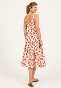 Robe midi florale sans manches, en tissu blanc avec de petites fleurs rouges, ourlet évasé et volants superposés en bas.