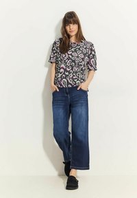 Černé a růžové proužkované tričko s krátkým rukávem spárované s modrými širokými džíny. Modelka nosí černé slip-on boty, ruce má v kapsách.