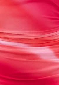 Gros plan d’un tissu avec un dégradé de tons rouges et roses montrant une texture fine en maille et des plis horizontaux.