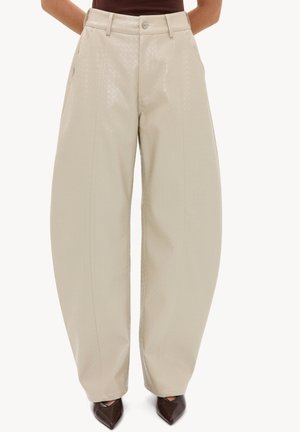 Pantalon ample taille haute couleur crème avec une texture subtile, porté avec des chaussures pointues foncées et un haut marron rentré.