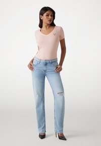 Lyserød v-hals t-shirt med logo detaljer, parret med lyseblå slidte brede jeans og sorte højhælede sko. Glat stof og afslappet pasform.