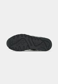 Juodas gumos sportinių batelių padas su tekstūruotomis sukibimo raštų ir "Reebok" logotipu, turintis iškilias apskritas formas ir griovelius sukibimui.