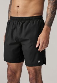 Shorts de sport noirs en tissu léger, dotés d'une taille élastique, de poches latérales et d'un petit logo sur l'ourlet.