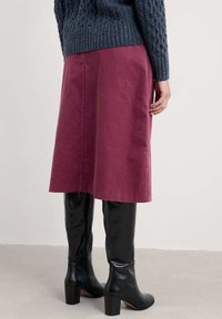 Bordeauxrok met een vloeiende uitstraling, gecombineerd met hoge zwarte leren laarzen met een blokhak. Erboven een gebreide donkerblauwe trui.