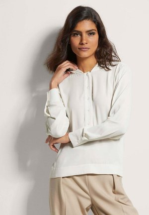 Lange mouw, licht crèmekleurige blouse van gladde stof met een knoopsluiting en opgevouwen kraag, gecombineerd met beige broek.