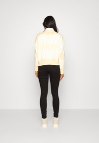 Sweatshirt em tie-dye amarelo claro e branco com bainha canelada, combinado com jeans skinny pretos e tênis de tom claro.