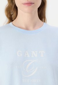 Heledsinine puuvillane T-särk, millel on ümar kaelus ja lühikesed varrukad. Omab valget logo trükki, millel on "GANT" ja allpool klassikalises serif-fontis detailid.