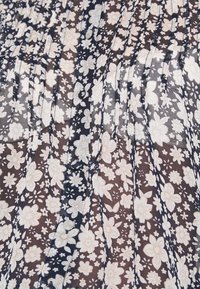 Tissu noir transparent avec imprimé floral blanc, comprenant des fleurs de petite et moyenne taille ainsi que des plis verticaux.