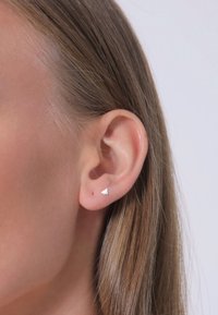 Boucle d'oreille triangulaire en argent avec une finition polie, présentée sur une oreille percée avec des cheveux bruns droits cascade au côté.
