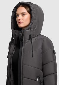 Gray puffer jacket with a large, adjustable hood, zippered front, and contrasting textured accents. Features side pockets and branding details.