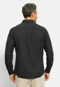 Black long-sleeve shirt with a smooth texture, buttoned cuffs, and a back pleat for fit, worn with light-colored corduroy pants.