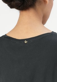 Black, short-sleeved shirt with a round neck and a small metallic heart accent at the back, highlighting a smooth texture and fitted design.
