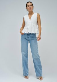 Top peplum blanco sin mangas con rayas verticales y botones, combinado con jeans rectos de color azul claro y sandalias de tiras plateadas.