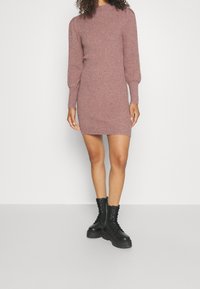 Robe en maille côtelée à manches longues de couleur mauve, avec un col montant et une silhouette cintrée. Associée à des bottines noires à lacets de style combat.