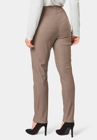 Bruine op maat gemaakte broek met een hoge taille en rechte pijpen. G gedragen met zwarte hoge hakken. Glad materiaal, minimale naden en geen zichtbare zakken.
