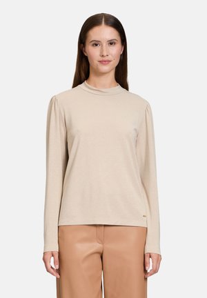Beige lange mouwtop met een hoge hals en geplooid schouderdetail, gemaakt van een zachte, licht gestructureerde stof, gecombineerd met tan broek.