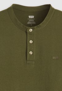Olivnozelena bombažna henley majica s tremi gumbi. Ima okroglo izrez in subtilno oznako Levi's na levi strani.