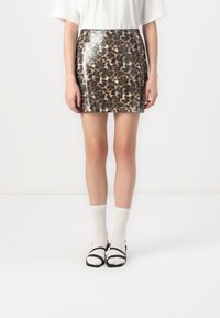 Minirok met luipaardprint en een glanzende afwerking, met een slank ontwerp in tinten bruin en zwart. Gecombineerd met witte kniekousen en zwarte schoenen.
