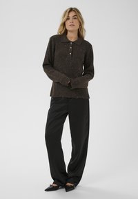 Brūna ribota garroku blūze ar apkakli un trim pogām, kopā ar melnām plata pieguļošām biksēm un smailu purngalu kurpēm. Smalkas mirdzošas detaļas.