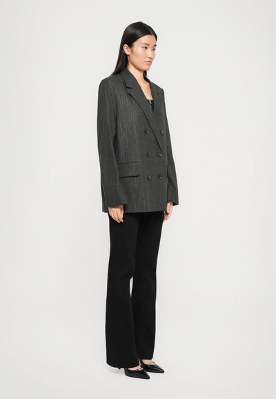 Blazer charcoal doppiopetto con righe verticali, ampie rever e due tasche frontali, abbinato a pantaloni neri svasati e scarpe a punta.