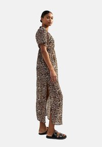 Maxi-jurk met luipaardprint, korte mouwen, een cinched taille, zijsplitten en doorschijnende stof. Gemaakt met zwarte sandalen met gespen.