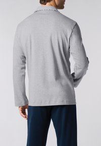 Camicia grigia a maniche lunghe con una texture morbida e dettagli a contrasto nel colletto, indossata con pantaloni blu navy, vista da dietro.