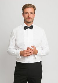 Weißes Hemd mit gefaltetem Vorderteil, schwarzer Fliege, französischen Manschetten und schlanker Passform. Tragen mit schwarzen formellen Hosen. Glatte Stofftextur.