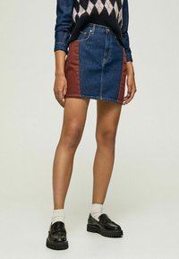 Jeansminikjol i mörkblått tyg med en brun sidopanel. Klassisk femfickdesign, ren sömnad och en figursydd silhuett.