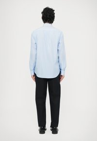 Světle modrá košile s dlouhým rukávem a jemným proužkovým vzorem, zaobleným lemem, manžetami na knoflíky a klasickým límečkem, nošená s černými kalhotami.